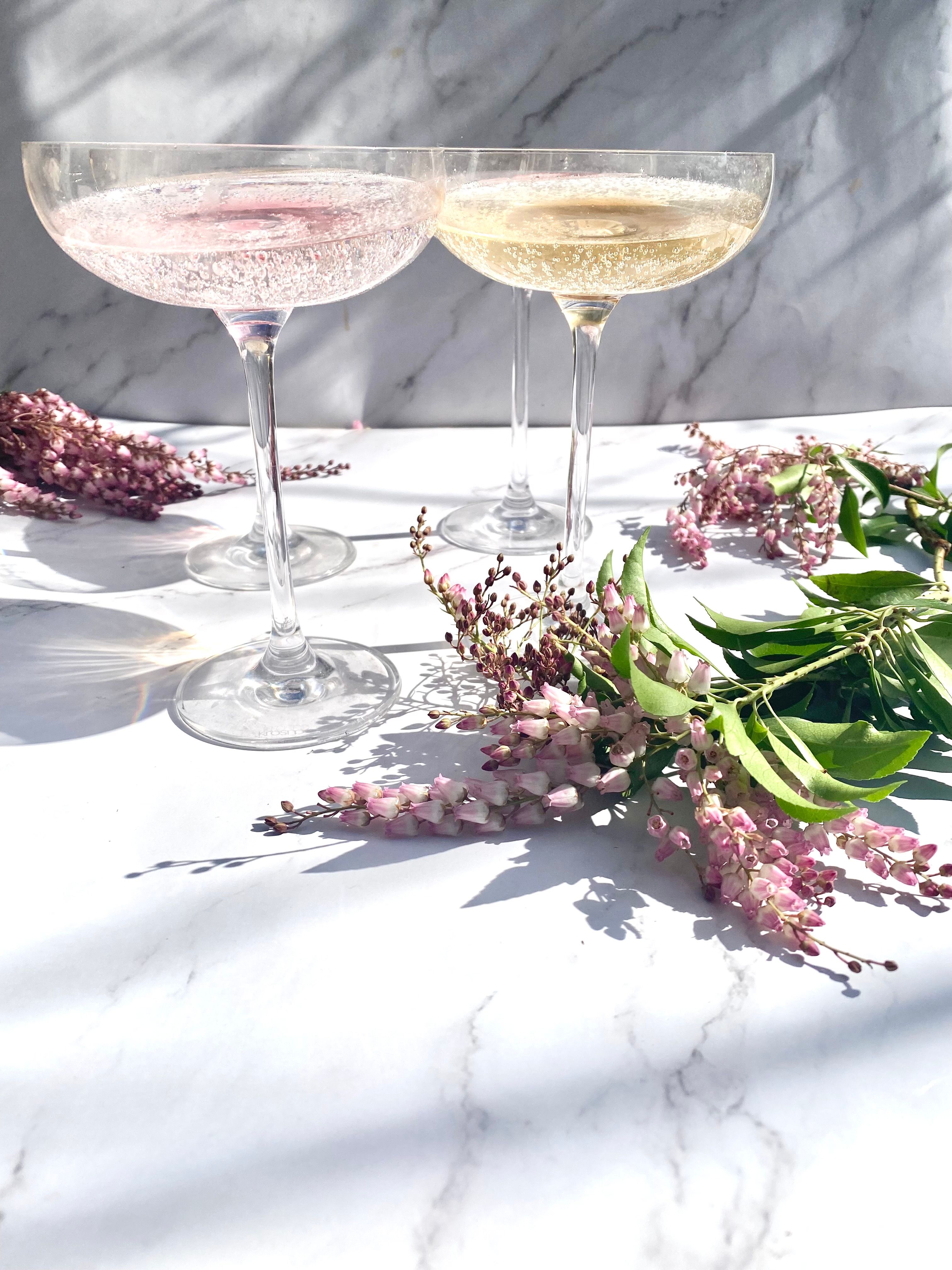Two sparkling wine glasses beside pink flowers